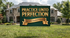 A green yard sign with gold lettering reading &