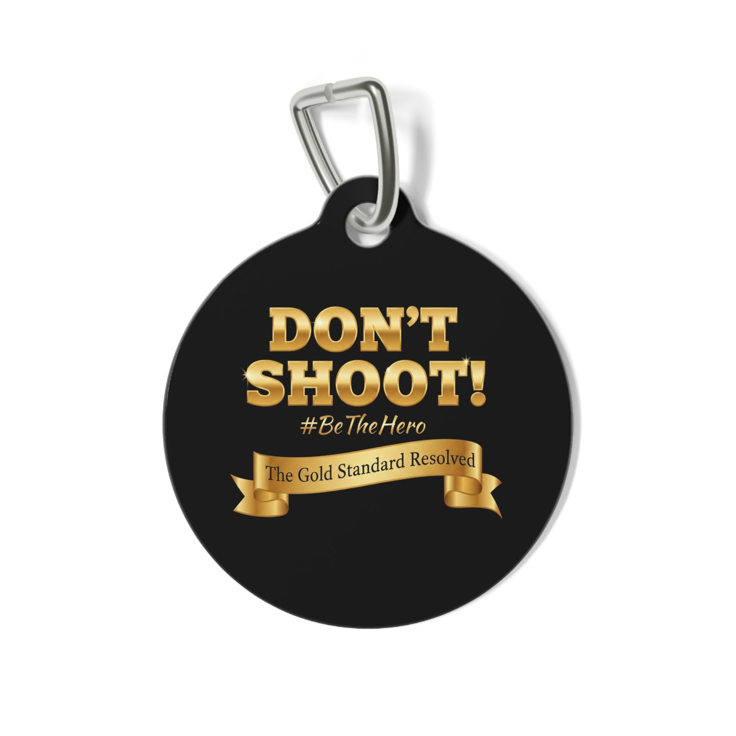 A round black pet ID tag with a silver metal clip, featuring the text 'DON'T SHOOT! #BeTheHero' and a gold ribbon banner that reads 'The Gold Standard Resolved' on a white background.
